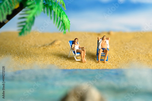 Fototapeta Naklejka Na Ścianę i Meble -  Miniature people toy figure photography. Men and girl couple relaxing on beach chair when daylight at seaside.