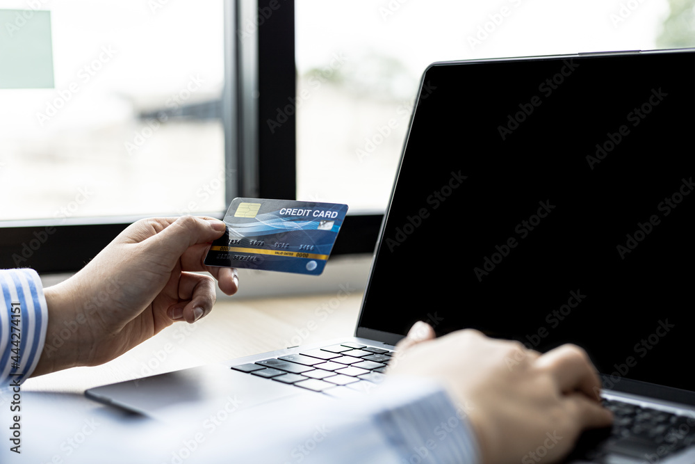 Woman typing on a laptop keyboard and holding a credit card, she fills in her credit card information on a laptop shopping app to pay for the order. Online shopping concept using credit card payments. Woman typing on a laptop keyboard and holding a credit card, she fills in her credit card information on a laptop shopping app to pay for the order. Online shopping concept using credit card payments.