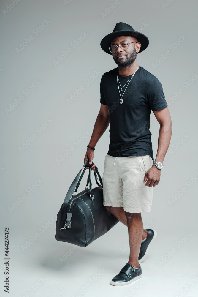 Handsome african american guy tourist in a hat holding a bag of luggage. Tourism concept Handsome african american guy tourist in a hat holding a bag of luggage. Tourism concept