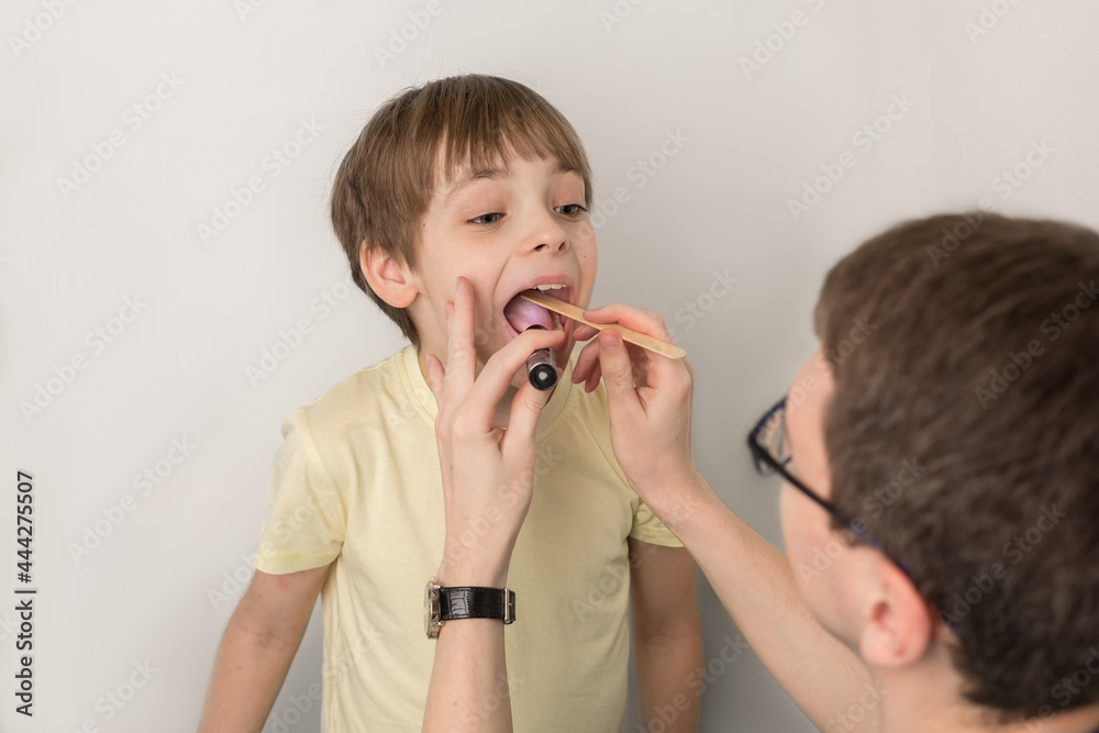 Examination of the throat, mouth and child by a doctor. The boy opened his mouth wide to examine his tonsils. Admission at the pediatrician Examination of the throat, mouth and child by a doctor. The boy opened his mouth wide to examine his tonsils. Admission at the pediatrician