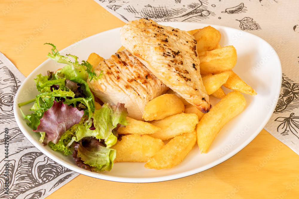 Grilled fried chicken breast fillets with a little lettuce and a side of French fries on a white plate