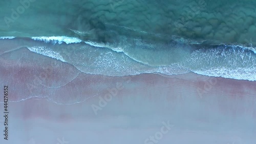 Top down aerial of Atlantic Ocean waves gently rolling in over a Florida beach at dawn. Muted colors of turquoise, grey, white, magenta, and tan.