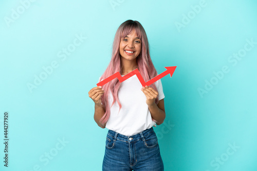 Young mixed race woman with pink hair isolated on blue background holding a catching a rising arrow with happy expression