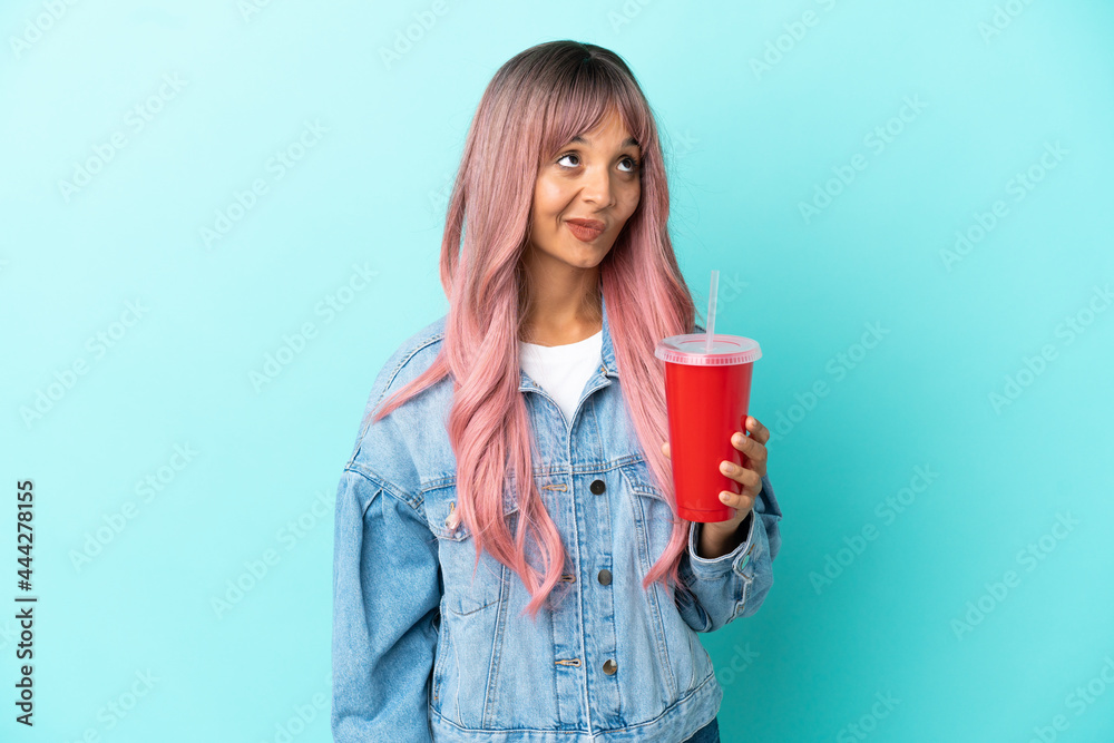 Young mixed race woman drinking a fresh drink isolated on blue background and looking up Young mixed race woman drinking a fresh drink isolated on blue background and looking up