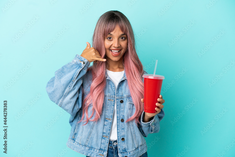 Young mixed race woman drinking a fresh drink isolated on blue background making phone gesture. Call me back sign Young mixed race woman drinking a fresh drink isolated on blue background making phone gesture. Call me back sign