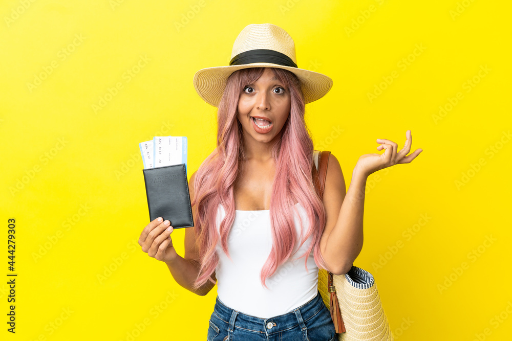 Young mixed race woman holding passport and beach bag isolated on yellow background with shocked facial expression