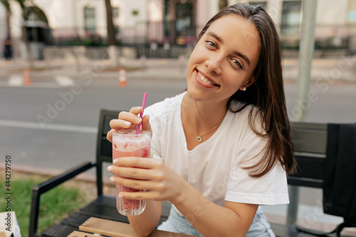 Pretty female model in white shirt laughing in good day. Attractive brunette woman with lemonade having fun outdoor.