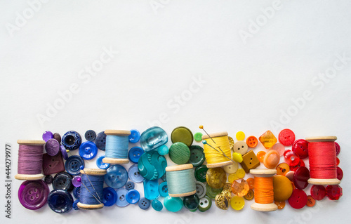 A lot of buttons and reels with colorful threads, laid out on a white background in the colors of the rainbow. Copy space