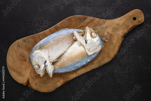 top view shot of steamed mackerel in olive natural wood cutting board on the dark tone texture background