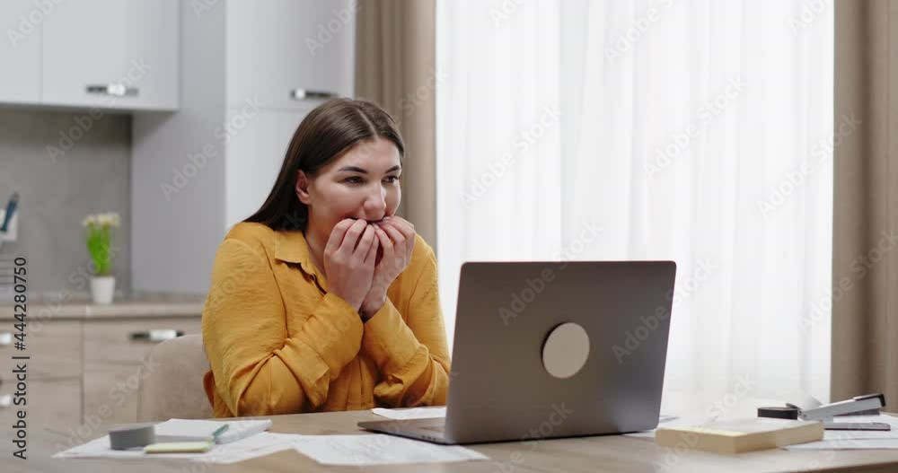 Young woman watching a horror movie on a laptop sitting at a table scared looking at the screen scared closes her face with her hands and closes the laptop