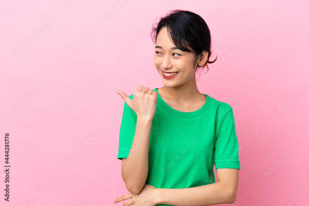 Young Vietnamese woman isolated on pink background pointing to the side to present a product Young Vietnamese woman isolated on pink background pointing to the side to present a product