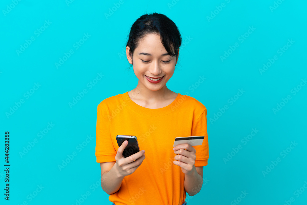 Young Vietnamese woman isolated on blue background buying with the mobile with a credit card Young Vietnamese woman isolated on blue background buying with the mobile with a credit card