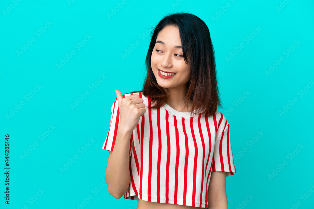Young Vietnamese woman isolated on blue background pointing to the side to present a product Young Vietnamese woman isolated on blue background pointing to the side to present a product