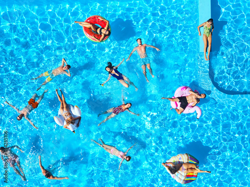 Aerial of friends having party in swimming pool with inflatable flamingo  swan  mattress. Happy young people relax at luxury resort on sunny day. View from above. Girls in bikini sunbathing in a sun.