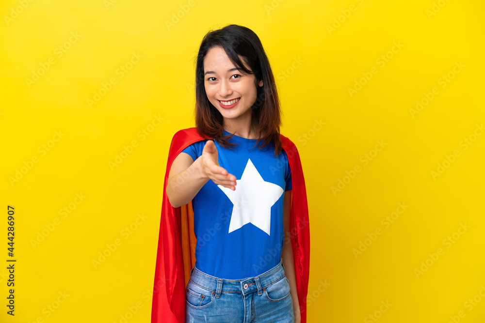 Super hero Vietnamese woman isolated on yellow background shaking hands for closing a good deal Super hero Vietnamese woman isolated on yellow background shaking hands for closing a good deal