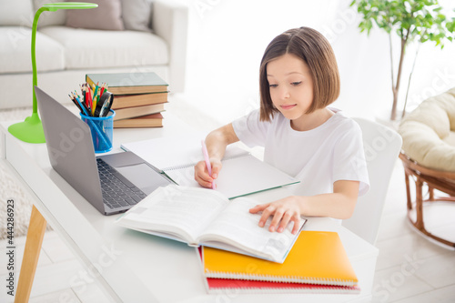 Photo portrait little girl writing homework in copybook reading book at table in room © deagreez