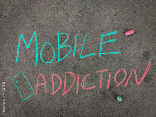 The inscription text on the grey board, Mobile addiction with hand drawn smart phone. Using color chalk pieces.