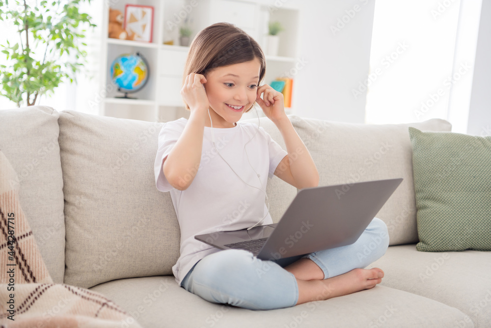Full length profile side photo of little girl happy positive smile wear headphones online lesson look laptop e-learning home Full length profile side photo of little girl happy positive smile wear headphones online lesson look laptop e-learning home