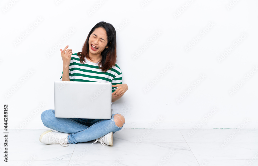 Young Vietnamese woman with a laptop sitting on the floor isolated on white wall making guitar gesture Young Vietnamese woman with a laptop sitting on the floor isolated on white wall making guitar gesture