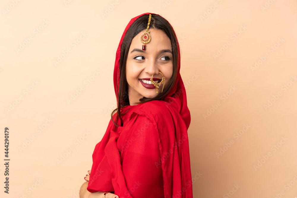 Young Indian woman isolated on beige background with arms crossed and happy Young Indian woman isolated on beige background with arms crossed and happy