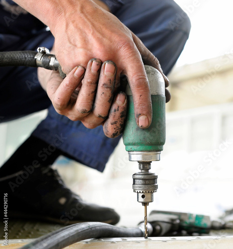 Worker hands making holes with a pneumatic drill on the body plane for further riveting photo