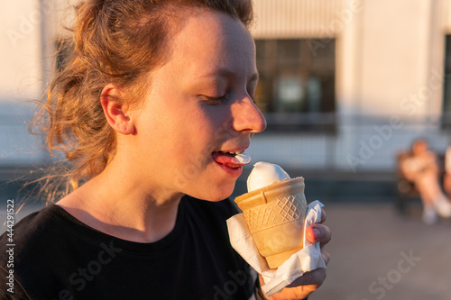 A young woman is holding, eating and enjoying an ice-cream cone
