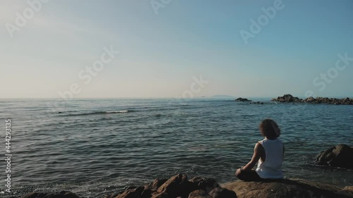 Man seated in meditation on a rock in front of the ocean