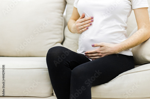 Cropped photo of pregnant female touching her stomach.