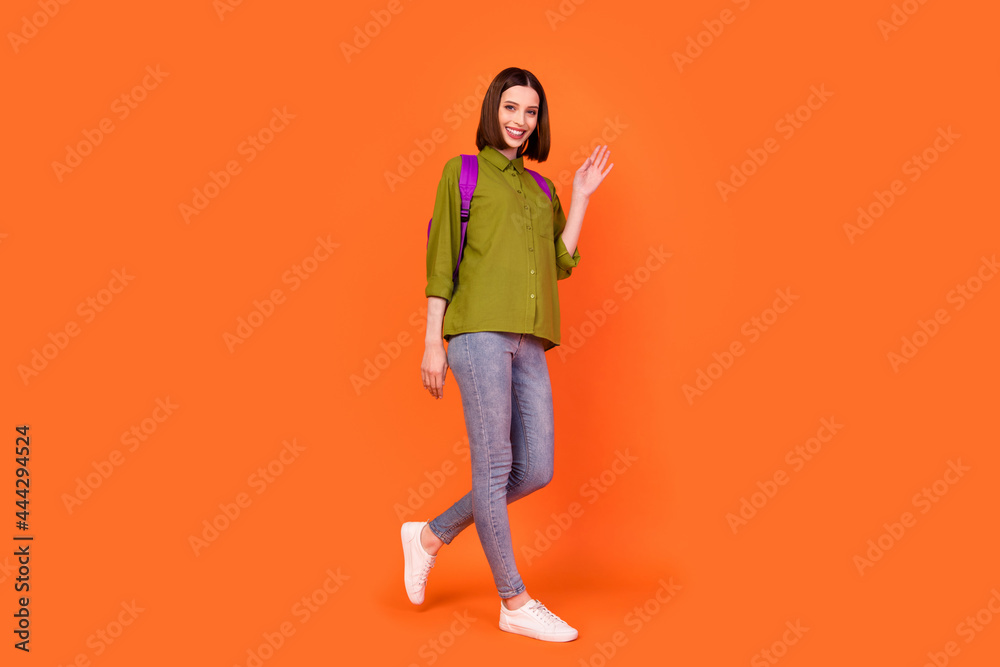 Full length photo of cute brunette young lady go wave wear bag shirt jeans isolated on orange color background Full length photo of cute brunette young lady go wave wear bag shirt jeans isolated on orange color background