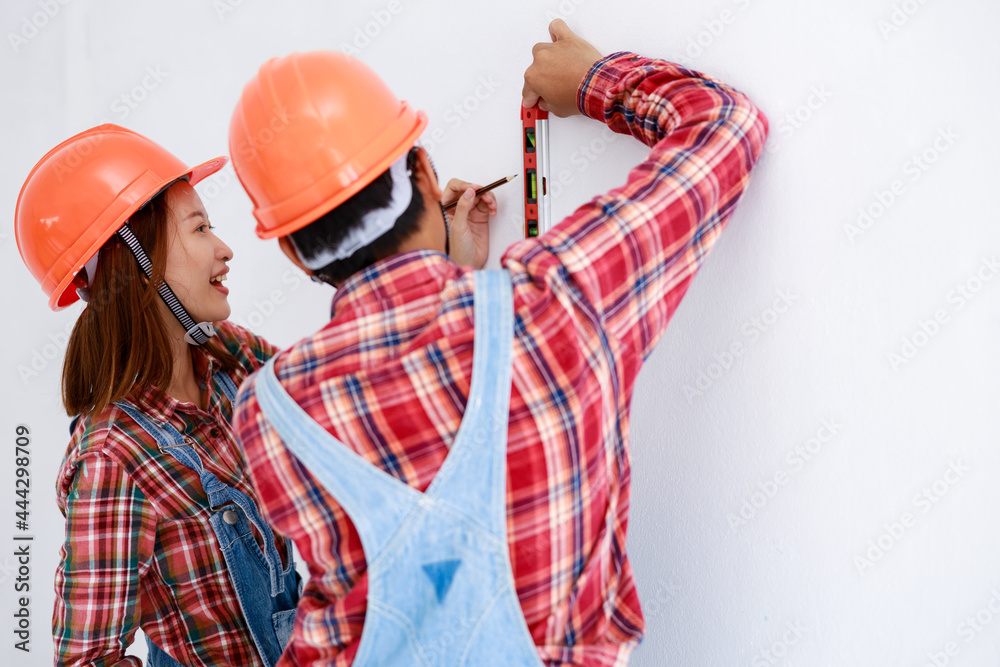 young asian couple in dress plaids shirt and bear cloth working and helping measuring the wall young asian couple in dress plaids shirt and bear cloth working and helping measuring the wall