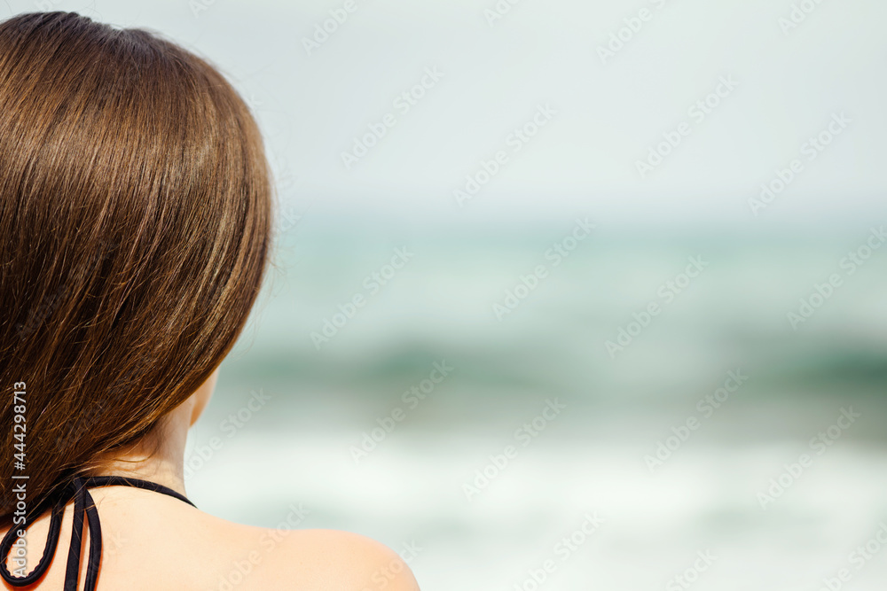 Alone woman on a beach looking on the sea. Female relaxation at summer vacation. Back view