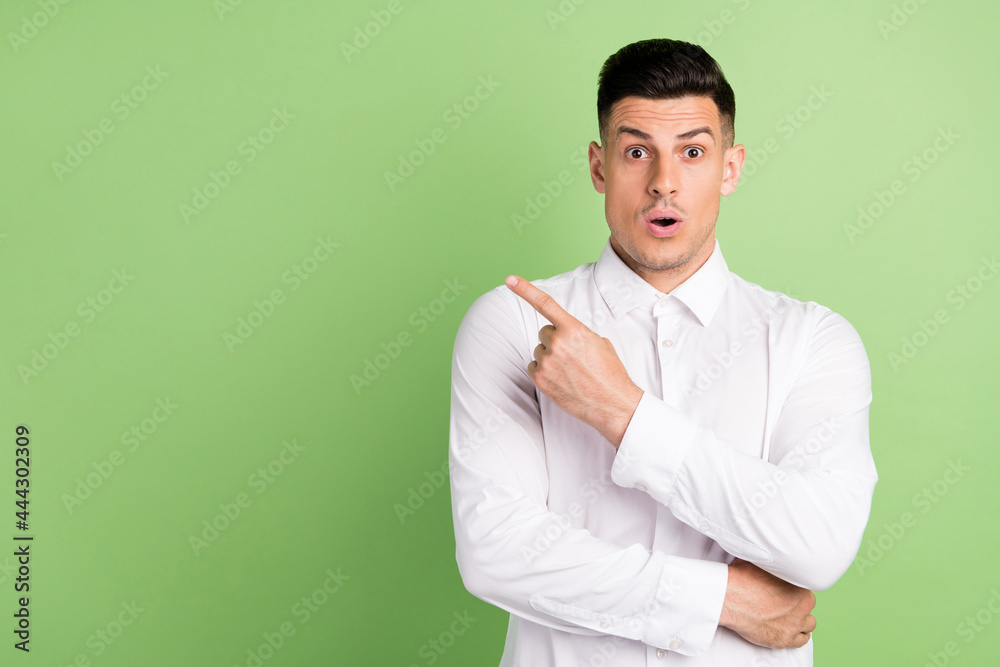 Photo of handsome impressed young guy dressed white shirt big eyes pointing finger empty space isolated green color background