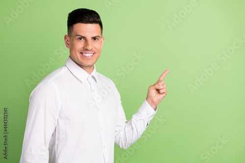 Photo of sweet charming young gentleman wear white shirt smiling pointing finger empty space isolated green color background