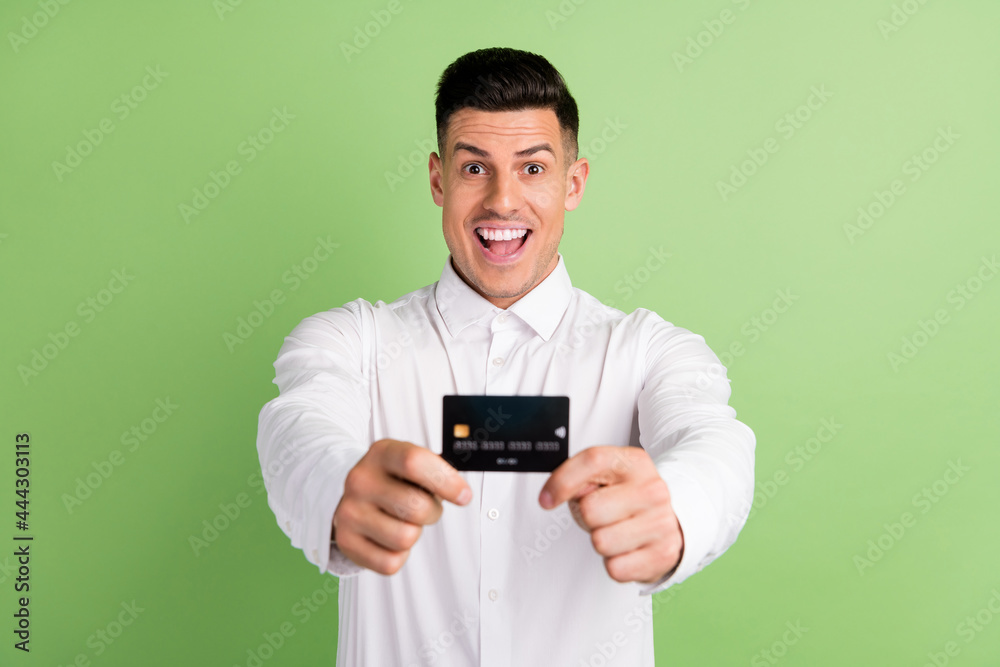 Photo of adorable pretty young guy dressed white shirt showing credit card open mouth smiling isolated green color background Photo of adorable pretty young guy dressed white shirt showing credit card open mouth smiling isolated green color background