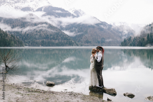 The concept of a wedding. A happy married couple in love in wedding clothes hugs stands in the middle of a boat pier a lake and misty mountains in nature in a fabulous place outdoors