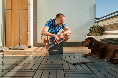 middle-aged man looking at his dog while setting up a new floor on his terrace