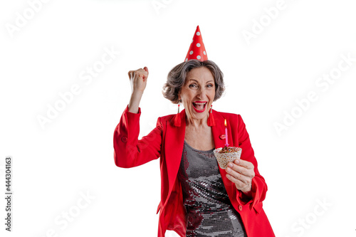 Senior woman holding birthday cake with candle wearing party hat