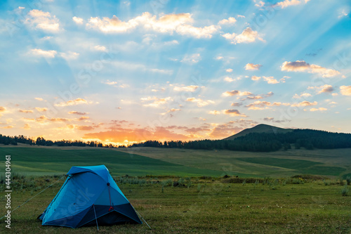 Beautiful summer landscape camp. The blue tent on green fields, mountains at the sunrise. Nature wallpaper