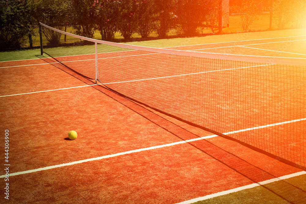 Wide angle photo of artificial grass tennis court with tennis ball during sunset.Competitive individual sports concept.