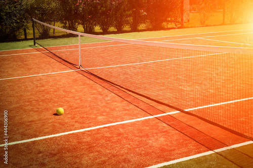 Wide angle photo of artificial grass tennis court with tennis ball during sunset.Competitive individual sports concept. © Myst