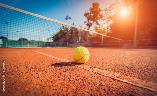 Wide angle close-up photograph of tennis ball on court during sunset. Competitive individual sports concept.  © Myst