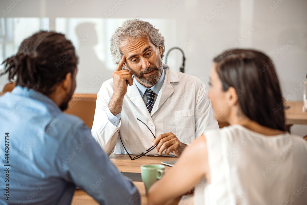 Obraz premium Cropped shot of a young couple having a consultation with their doctor. Shot of a doctor having a consultation with a couple in a clinic. Young couple during the consultations at clinic.