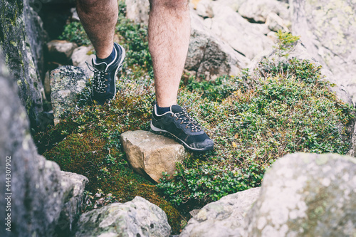 Guy hiking in comfortable hiking boots. Boots close-up stock photo. Trail runner climbing a steep rock in his path.