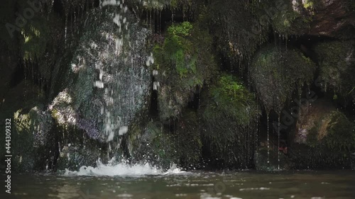 Slow motion video of waterfall running through mossy stones and water splashing in a lake