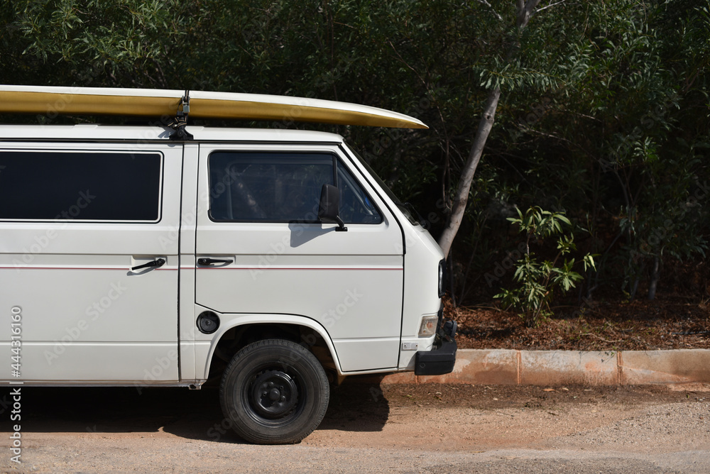 old camper van with surfboard on rooftop on forest background