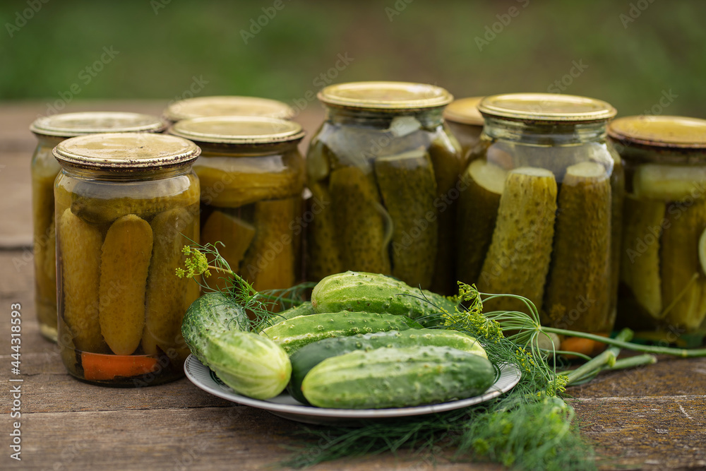 Glass jars with canned cucumbers in a rustic style on a wooden table. Plate with fresh cucumbers and dill Glass jars with canned cucumbers in a rustic style on a wooden table. Plate with fresh cucumbers and dill