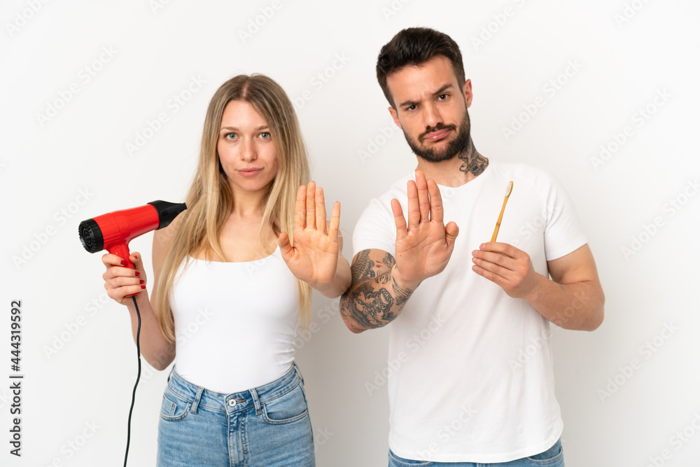 Couple holding a hairdryer and brushing teeth over isolated white background making stop gesture denying a situation that thinks wrong Couple holding a hairdryer and brushing teeth over isolated white background making stop gesture denying a situation that thinks wrong