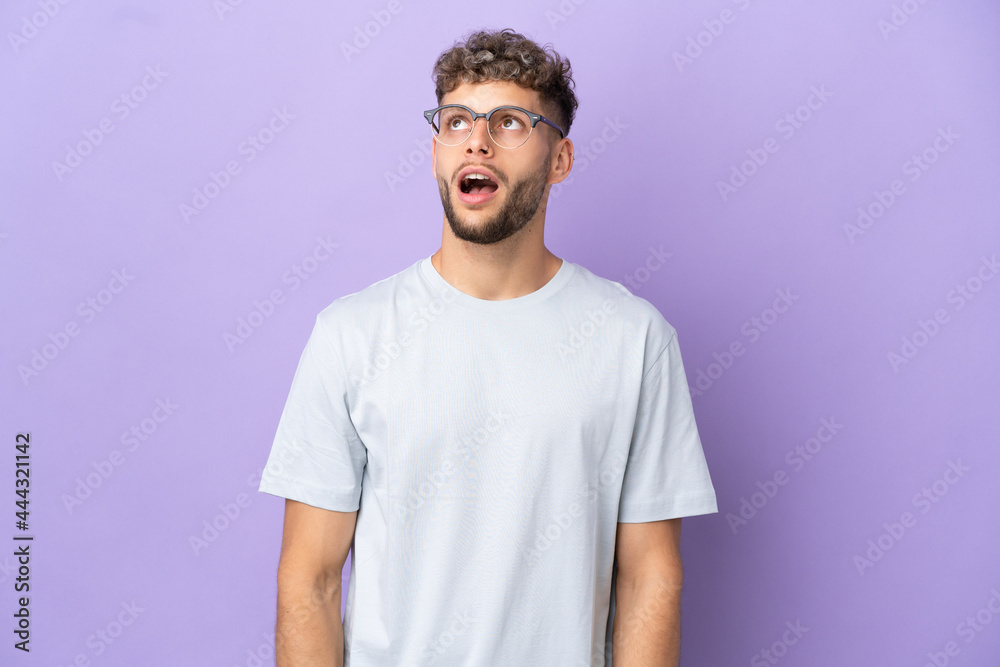 Delivery caucasian man isolated on purple background looking up and with surprised expression Delivery caucasian man isolated on purple background looking up and with surprised expression