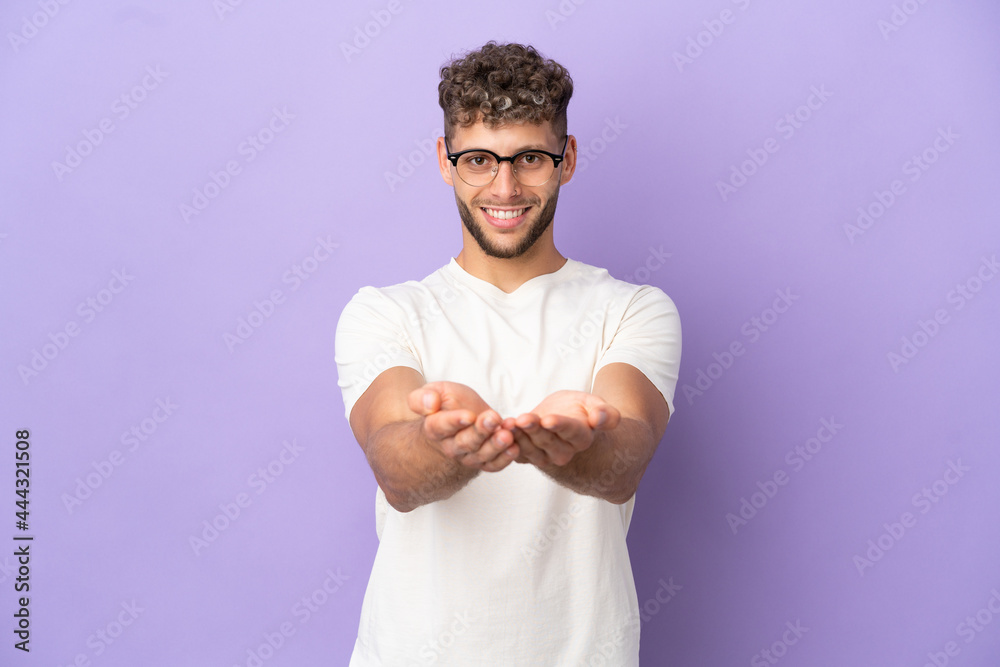 Delivery caucasian man isolated on purple background holding copyspace imaginary on the palm to insert an ad Delivery caucasian man isolated on purple background holding copyspace imaginary on the palm to insert an ad