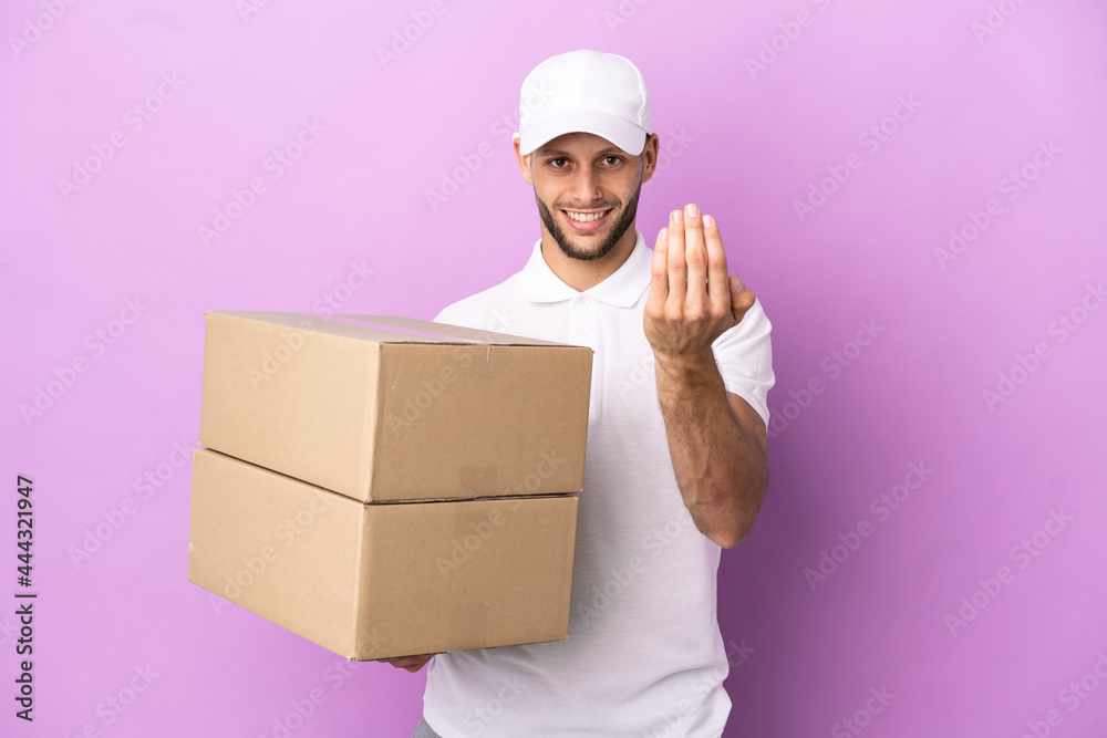 Delivery caucasian man isolated on purple background inviting to come with hand. Happy that you came Delivery caucasian man isolated on purple background inviting to come with hand. Happy that you came